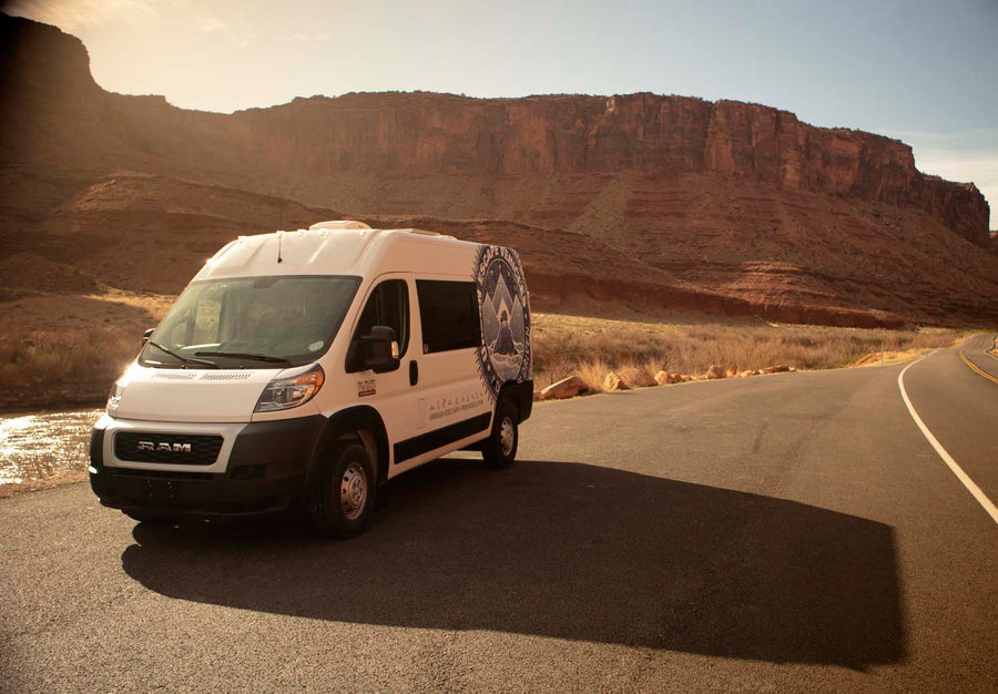 White **rv rental** camper van on a desert road, bathed in warm light, surrounded by majestic red rock canyons and a river.