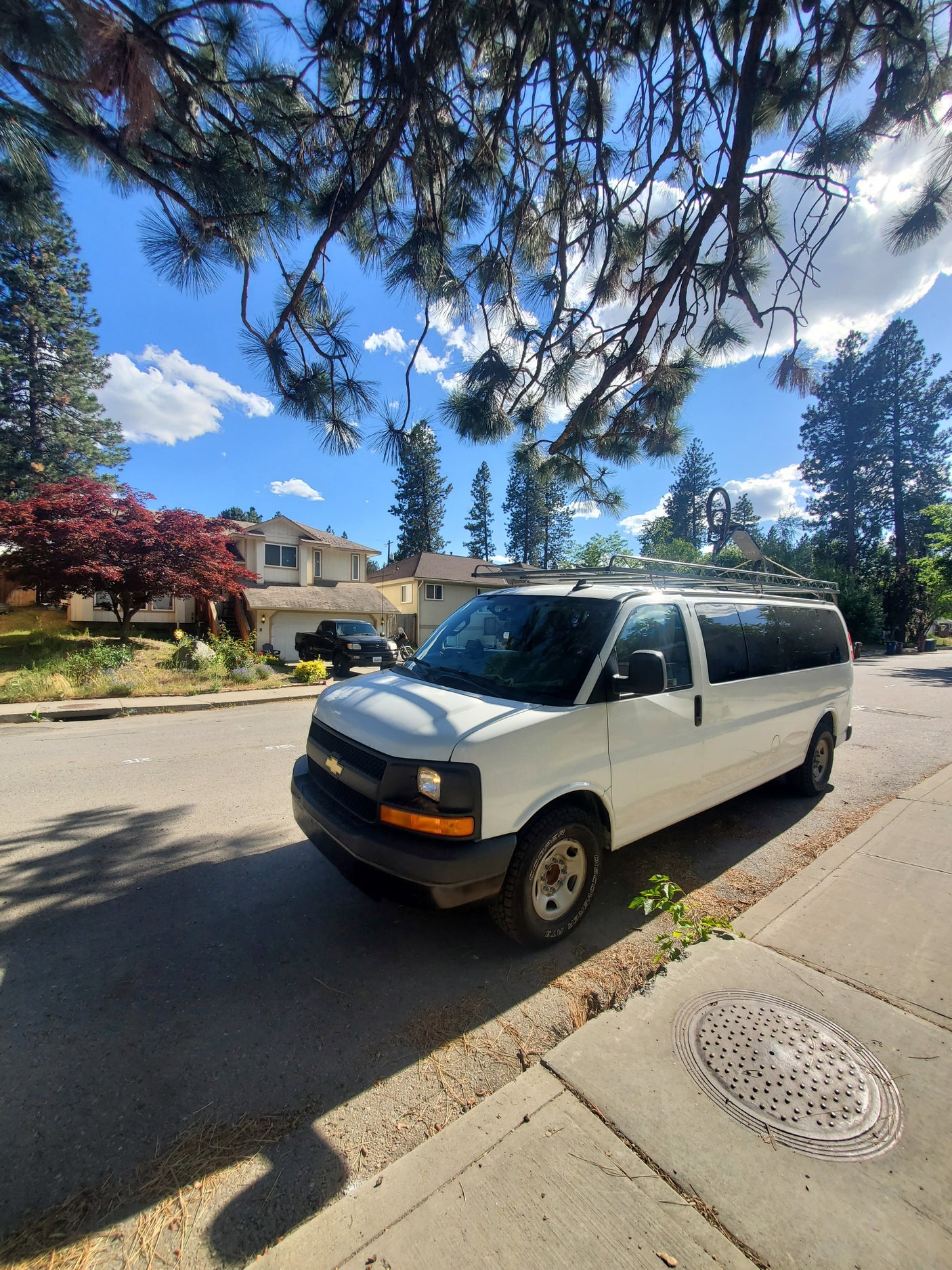 A white van with a roof rack parked on a sunny residential street with trees and houses, often converted for rv rental use.