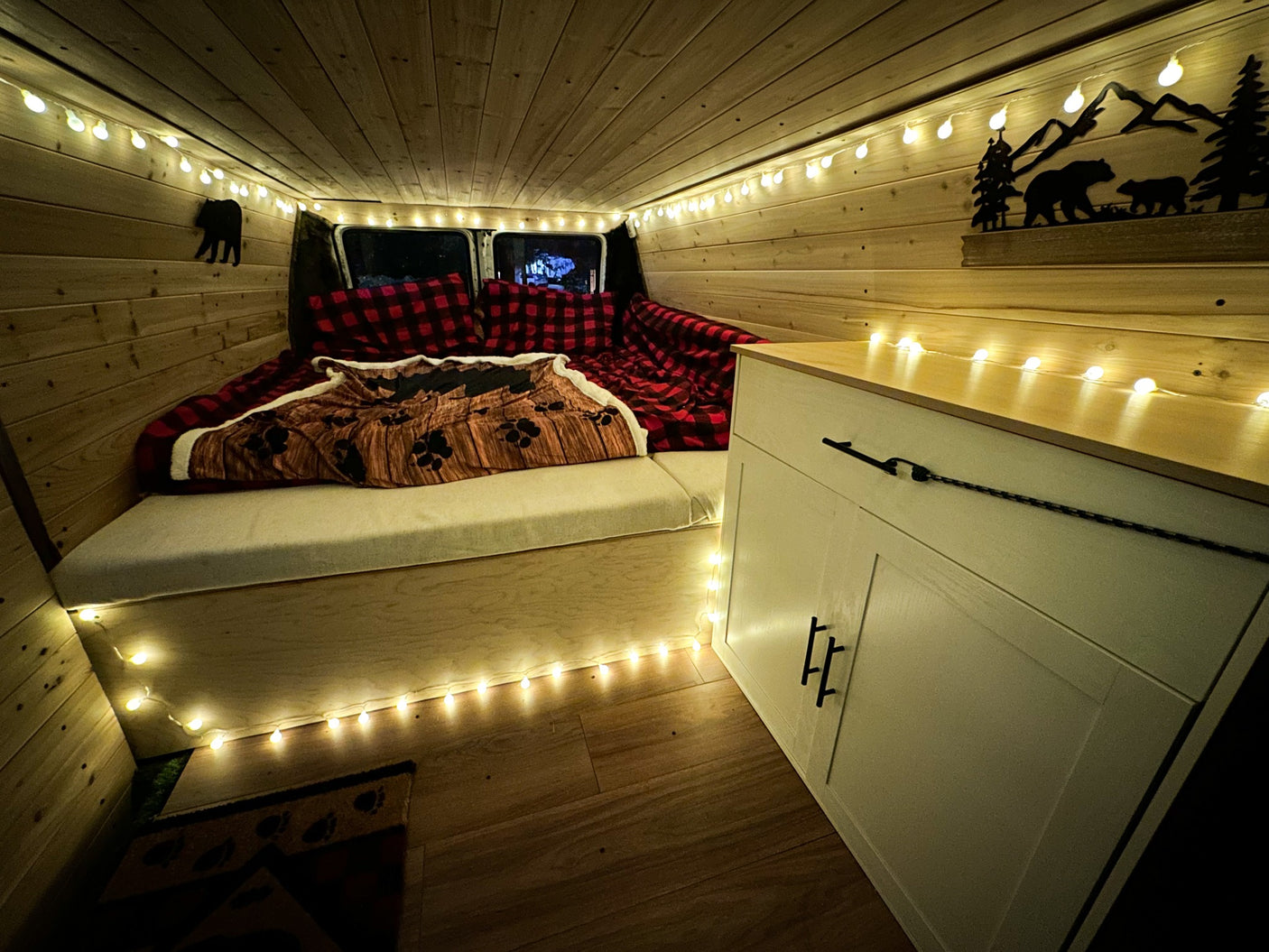 Experience cozy van life with this RV rental! Wood interior, string lights, and comfy bed with bear accents.