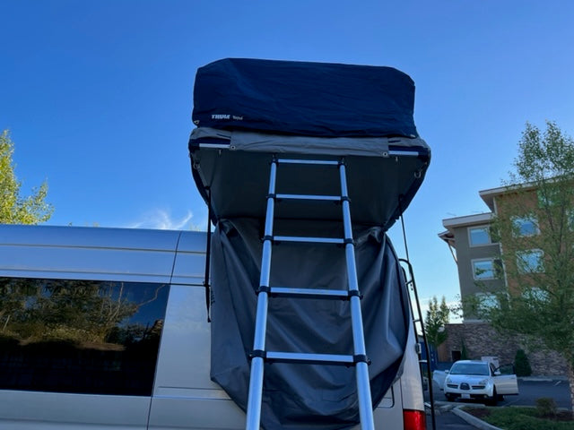 Back view of an RV rental van with a ladder leading to a deployed Thule rooftop tent for camping.