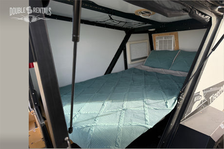 Cozy interior of an rv rental camper: a teal bed, pillows, and an AC unit. Perfect for comfortable mobile lodging.