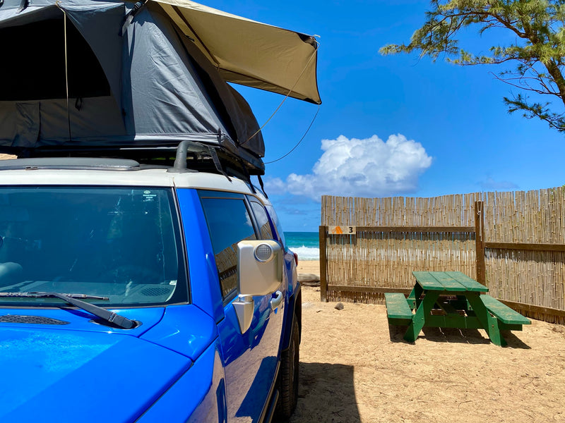 RV rental: Blue SUV with rooftop tent ready for beach camping. Sunny day with ocean view & picnic table. — photo 4