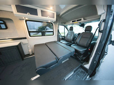 Explore this versatile RV rental camper van interior. Features a convertible bed, cozy front seats, and overhead storage.