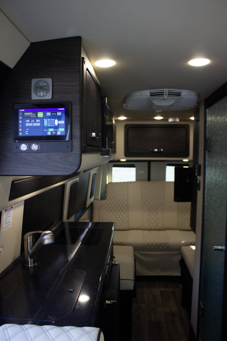 Modern rv rental interior with smart control panel, sleek kitchen, and plush quilted rear seating.
