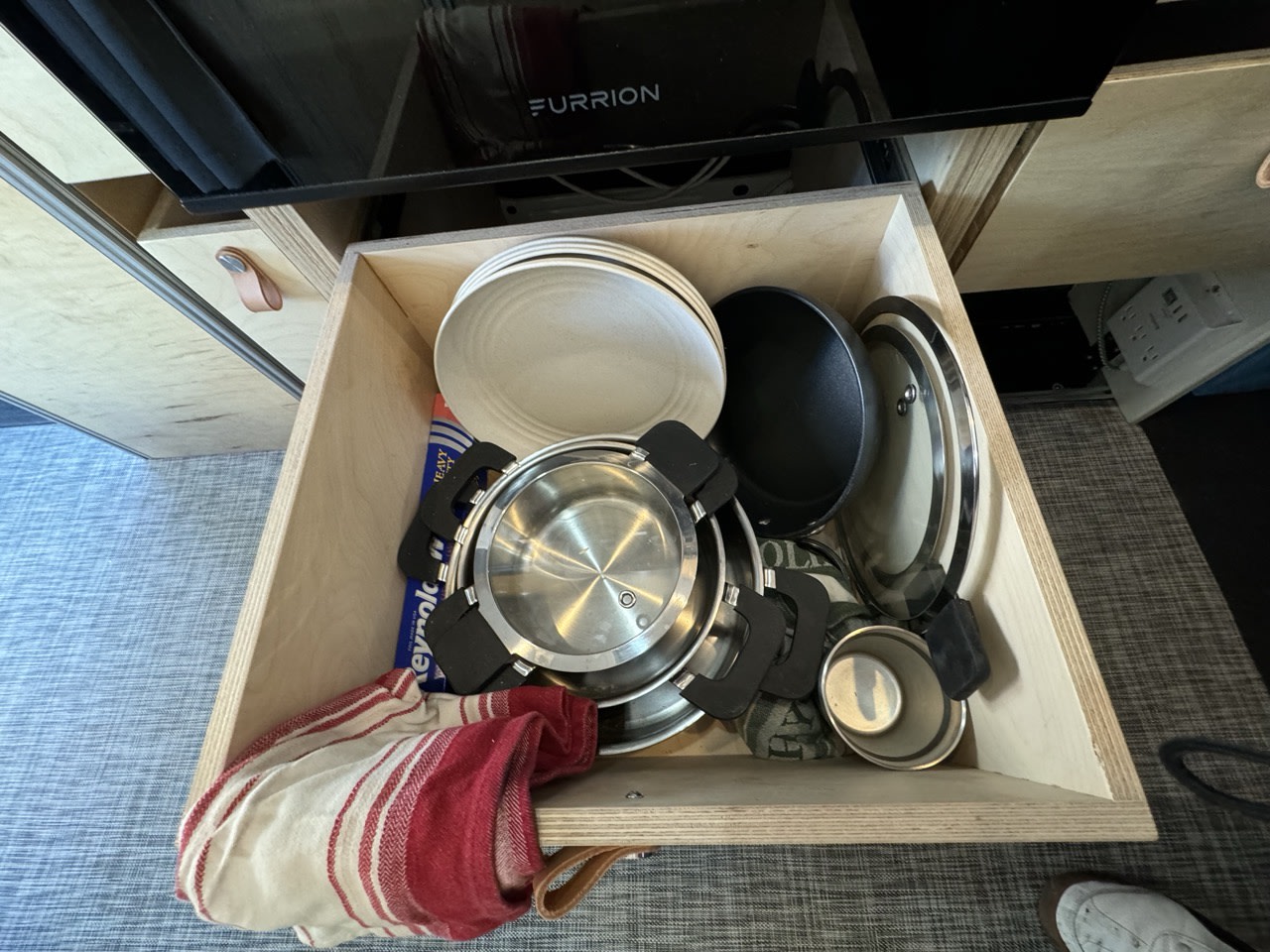RV rental kitchen drawer organized with plates, pots, pans, and a towel for travel cooking essentials.