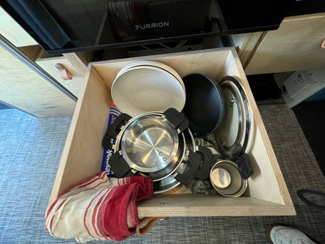 RV rental kitchen drawer organized with plates, pots, pans, and a towel for travel cooking essentials.