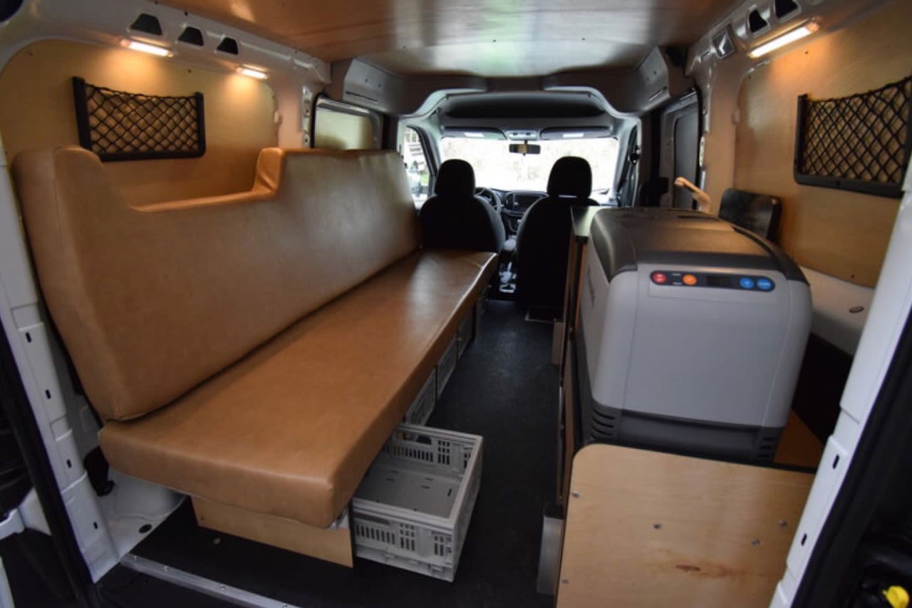 RV rental: Converted van interior with long bench seating, under-seat storage, and large portable fridge.
