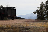 Overland RV rental trailer at a picturesque Colorado mountain campsite with snow-capped peaks. Perfect for outdoor adventure.
