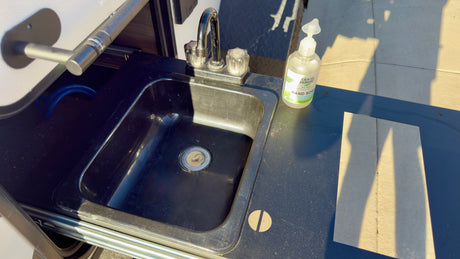 RV rental: Outdoor kitchen with a black sink, chrome faucet, and hand soap on a dark counter, perfect for camp use.