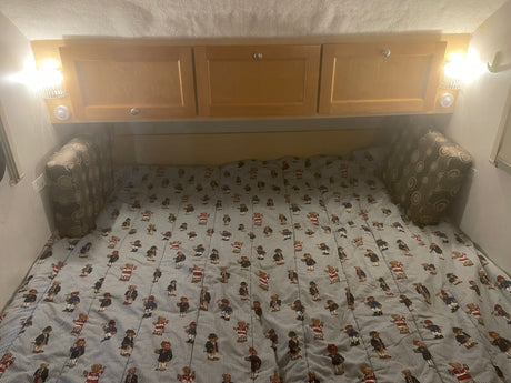 Inside an RV rental: a cozy bed with teddy bear striped comforter, overhead cabinets, and reading lights.