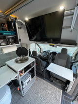 Inside a modern RV rental, featuring a compact kitchenette, large TV, swivel table, and the driver's area.