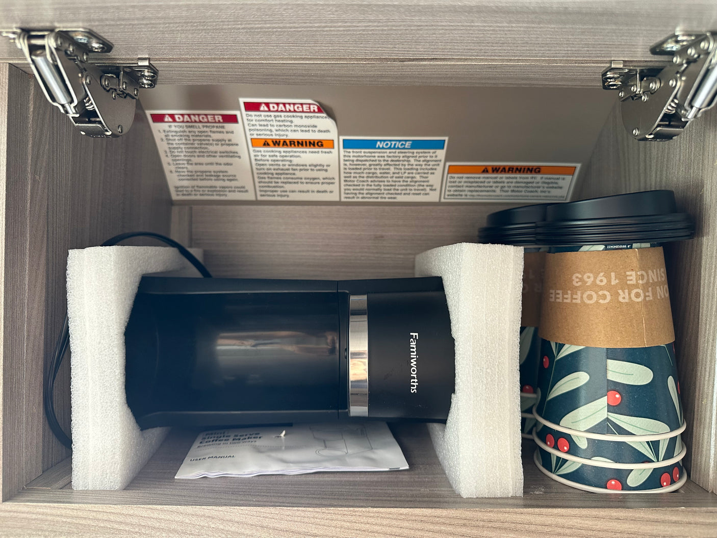 Inside an RV rental cabinet: a new Famiworths single-serve coffee maker (in foam) with stacked cups.