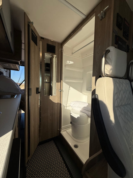 Inside this rv rental: A compact bathroom with toilet and shower, a bed, and the front cabin area are visible.
