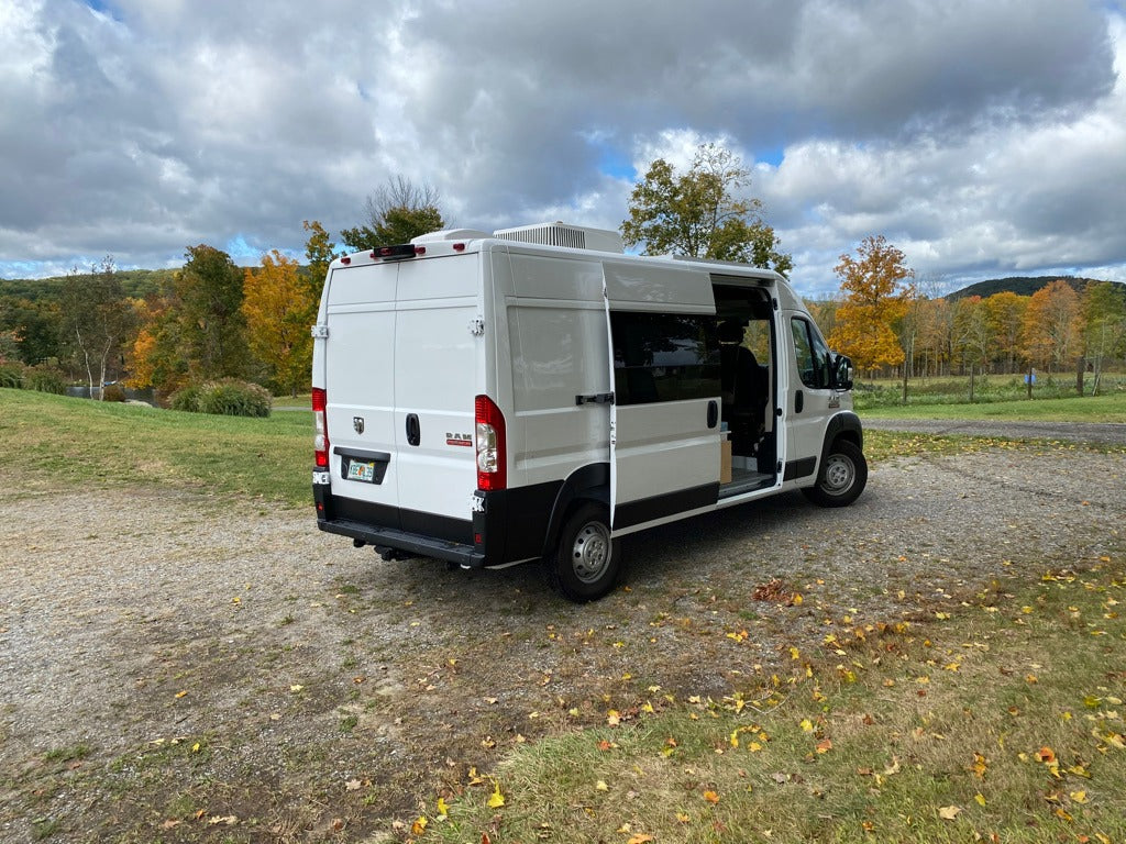White Ram ProMaster camper van RV rental with open side door, parked in an autumn landscape with colorful trees.