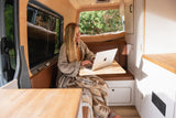 Cozy RV rental: woman working on laptop inside a stylish camper van, enjoying nature. Perfect for remote work & travel.