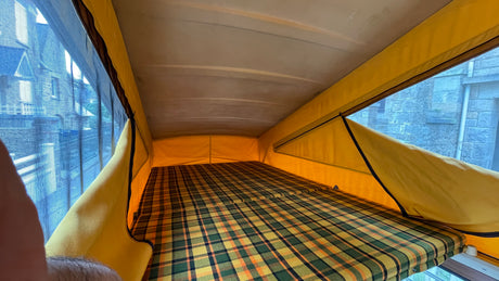Inside an RV rental: a pop-top campervan sleeping area with a vibrant plaid mattress, offering a cozy retreat.