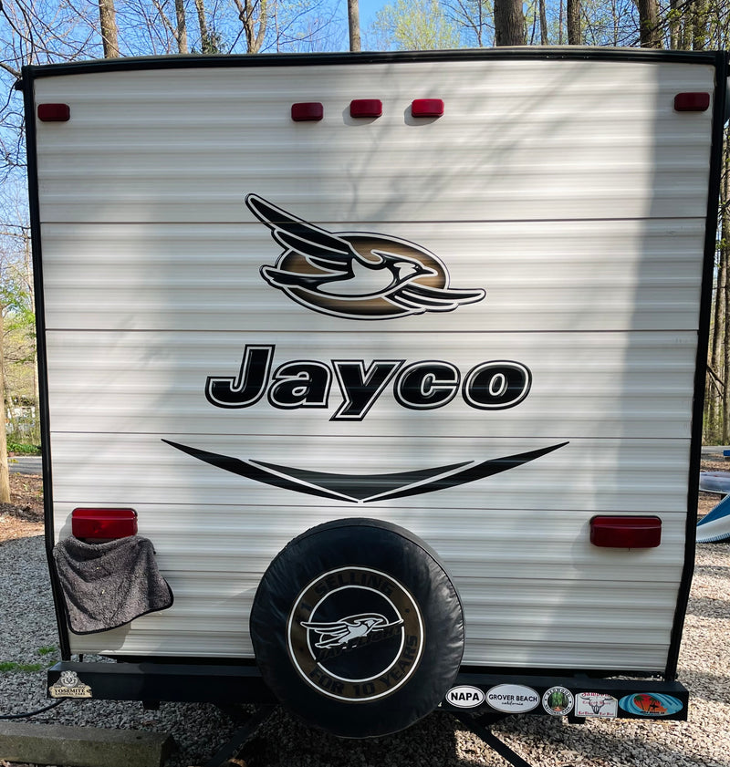 Back of a white Jayco travel trailer, often an RV rental, showing its spare tire, taillights, and travel stickers at a campsite. — photo 14