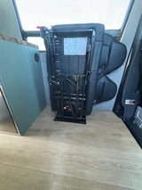 An RV rental interior features a black foldable seat/bed mechanism stowed, next to teal cabinets on light wood-look flooring.