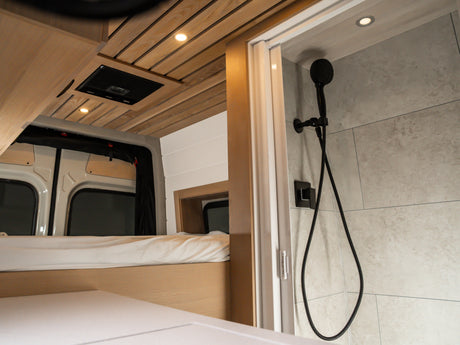 Enjoy a modern RV rental featuring a comfortable bed, beautiful wooden ceiling, and a compact, stylish shower area.