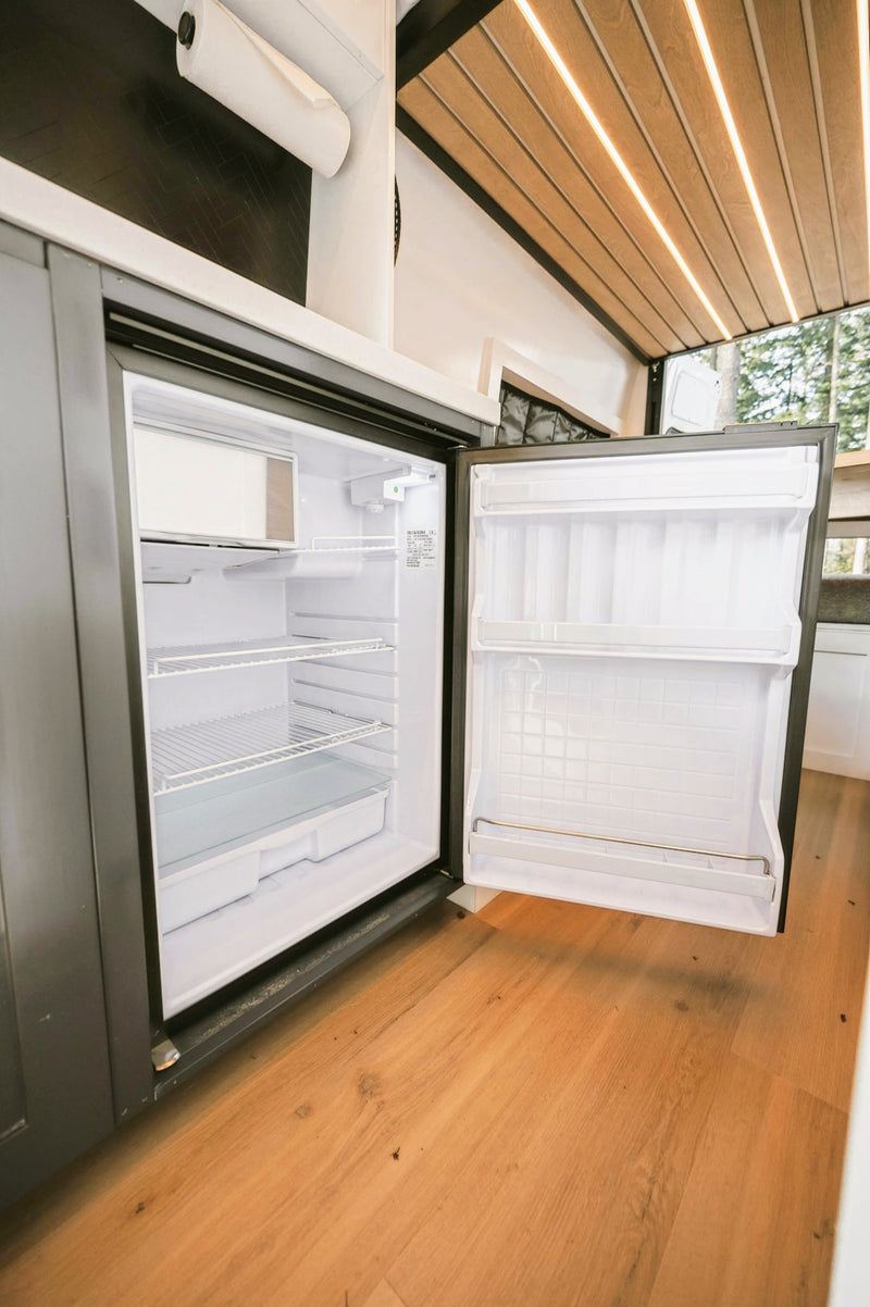 Empty compact refrigerator inside a modern RV rental, showing shelves, freezer, and door storage. — photo 20