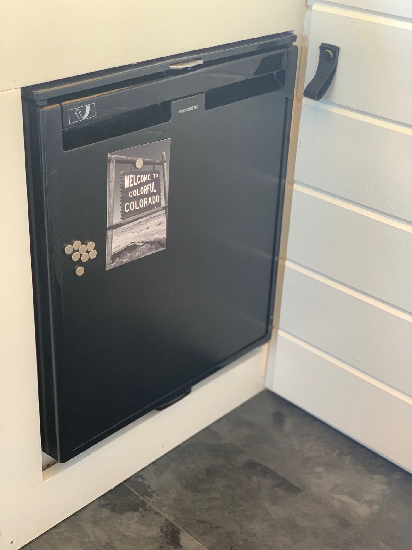 Built-in Dometic fridge in an RV rental, adorned with a Colorado magnet and others, offering compact storage.