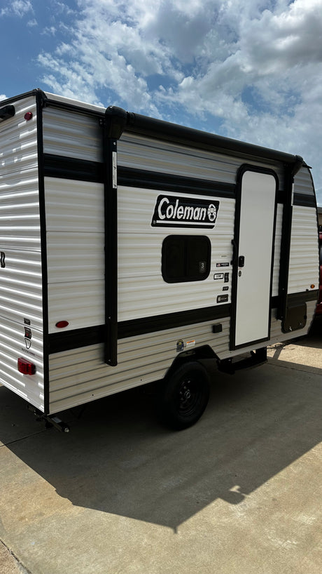 This Coleman travel trailer, ideal for an rv rental, is parked outside on a sunny day. Its white and grey exterior and awning hint at outdoor adventures.