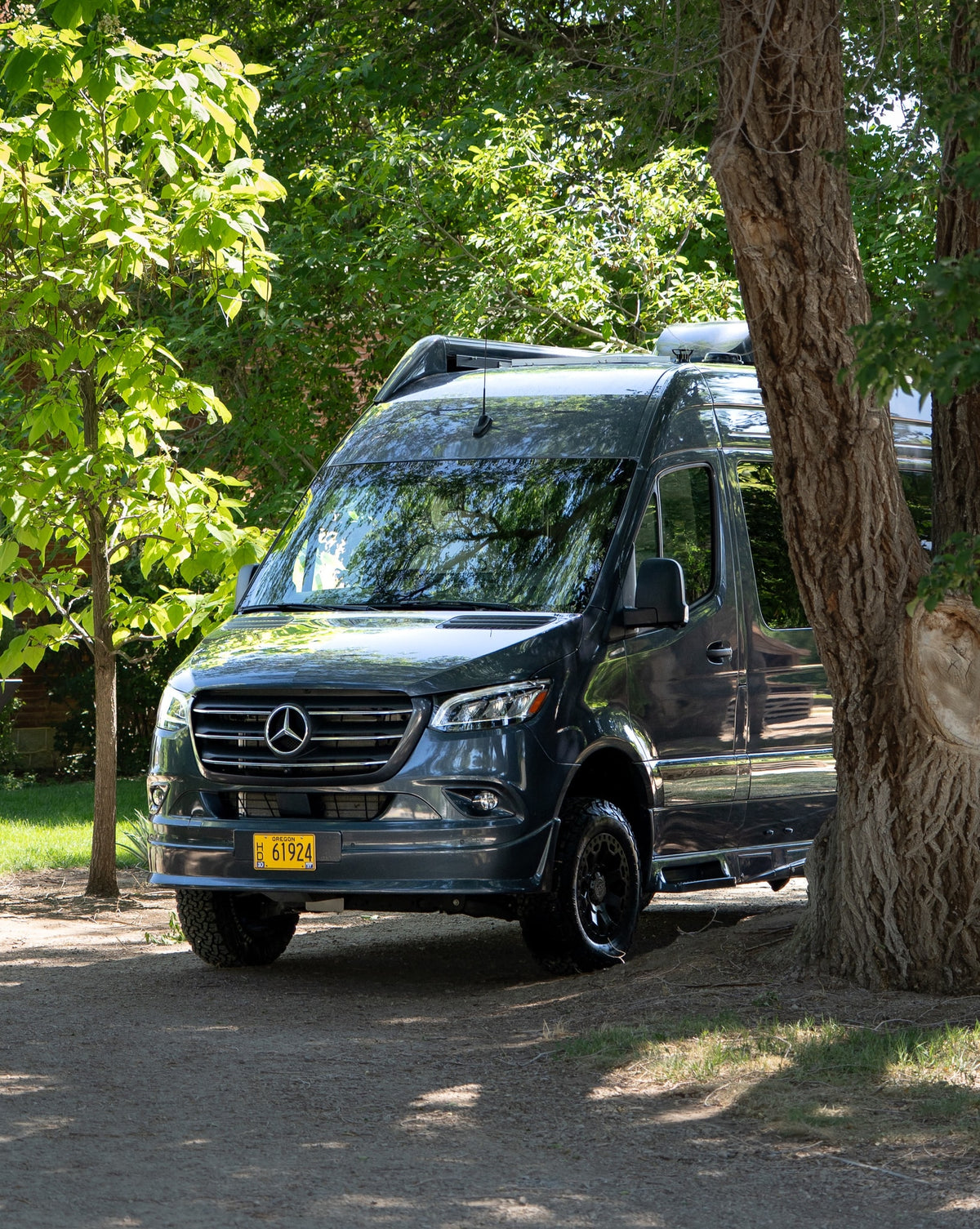 Stylish dark gray Mercedes-Benz Sprinter rv rental parked under lush green trees, ideal for outdoor travel. — photo 4