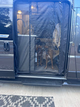 An RV rental's mesh screen door reveals two brown dogs and a cozy interior with a sink, perfect for pet-friendly adventures.