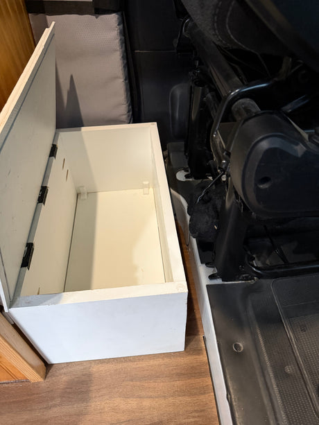 RV rental interior: open white storage bin for organization, situated on wood flooring by a vehicle seat.