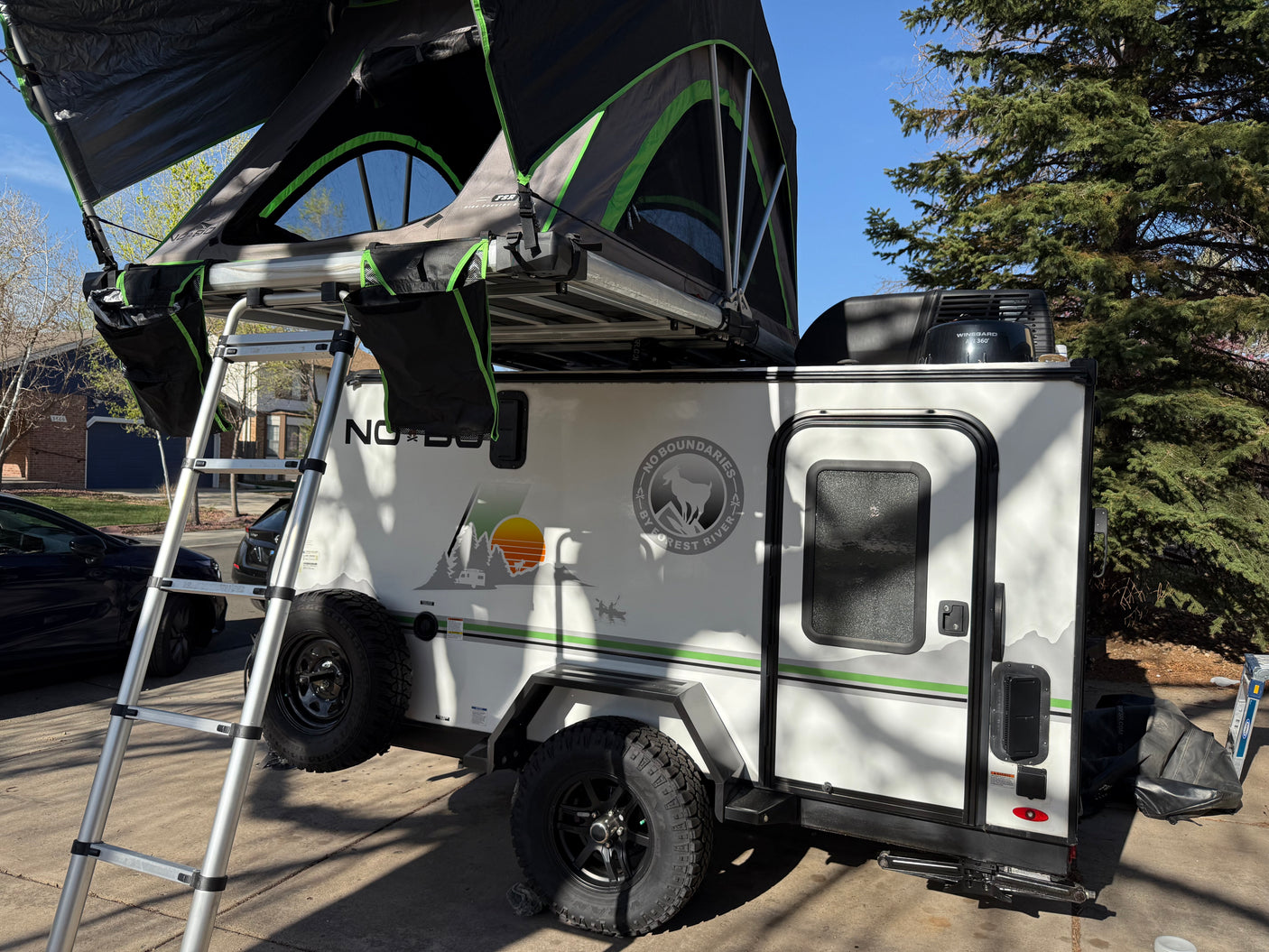 Adventure-ready RV rental: White travel trailer featuring a rooftop tent, ladder, and off-road tires.
