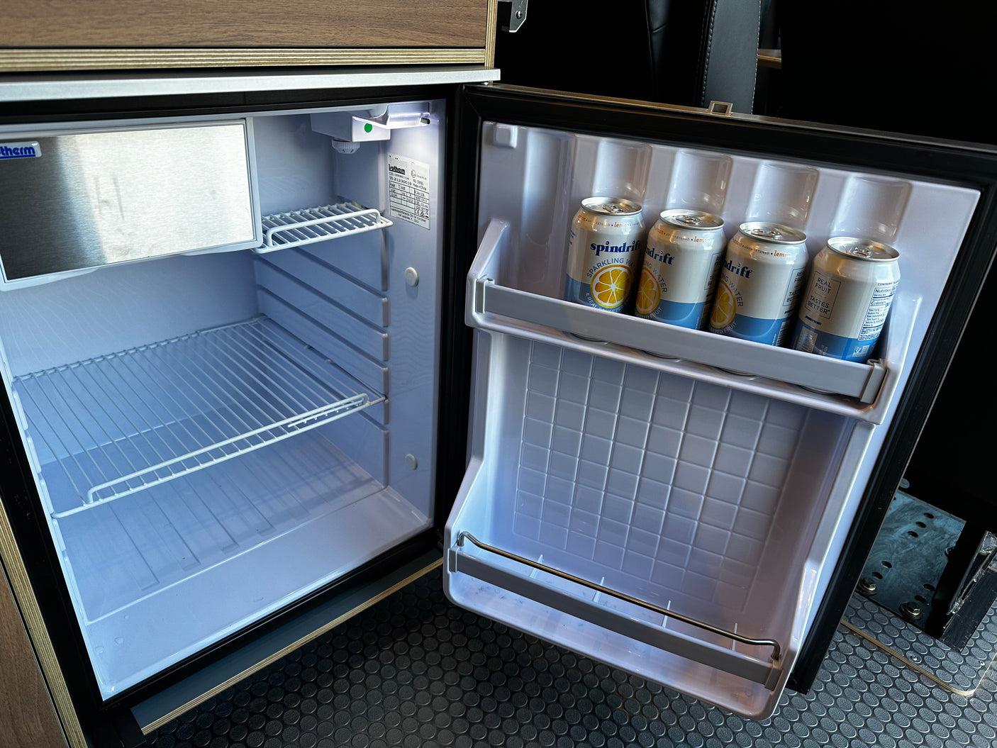 Open RV rental mini-fridge with empty shelves and door holding lemon Spindrift sparkling water cans.