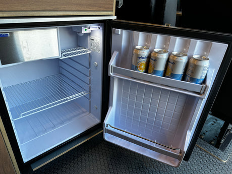 Open RV rental mini-fridge with empty shelves and door holding lemon Spindrift sparkling water cans.