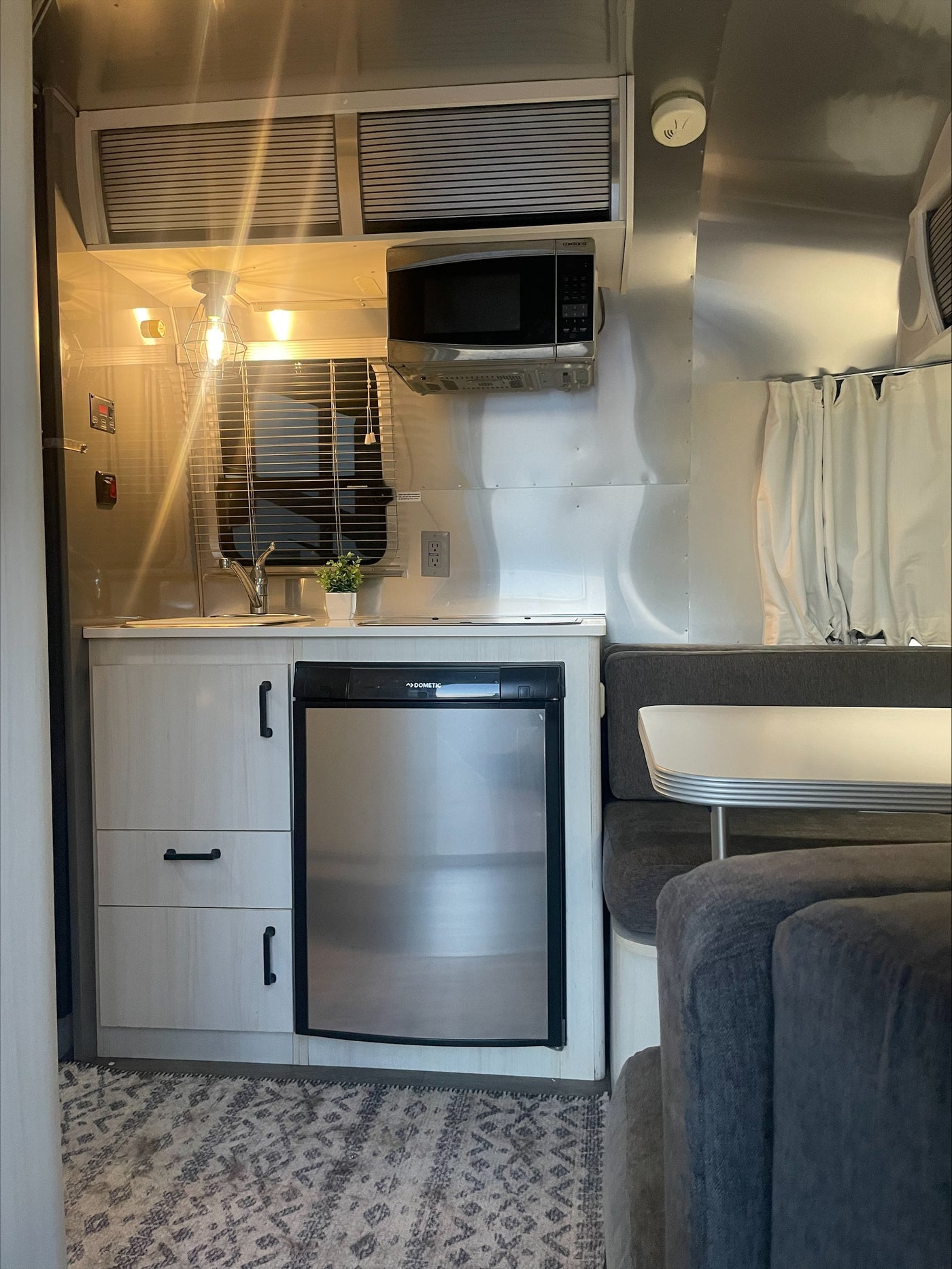 Cozy RV rental interior with a compact kitchen including a Dometic fridge, microwave, and a comfortable dining lounge. — photo 3