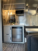 Cozy RV rental interior with a compact kitchen including a Dometic fridge, microwave, and a comfortable dining lounge.