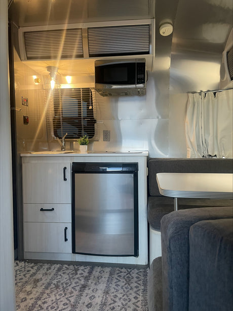 Cozy RV rental interior with a compact kitchen including a Dometic fridge, microwave, and a comfortable dining lounge.