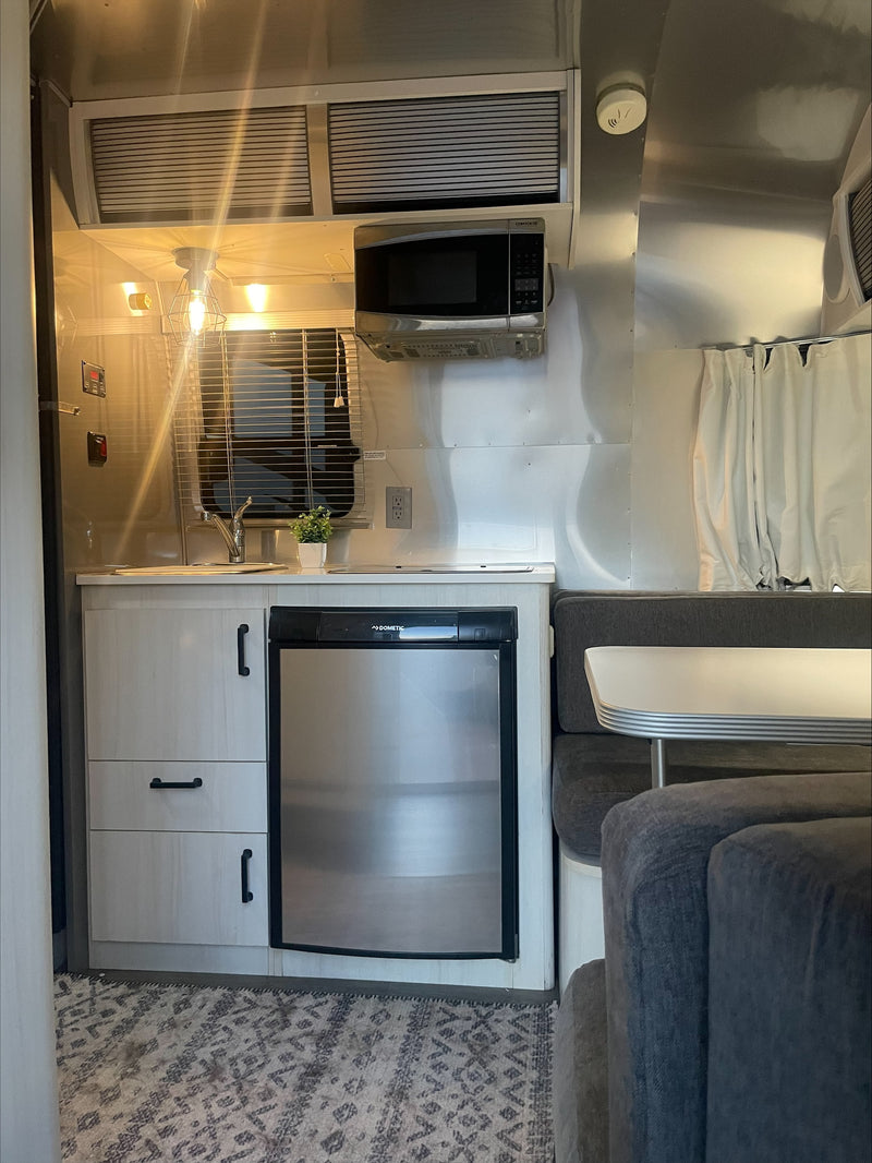 Cozy RV rental interior with a compact kitchen including a Dometic fridge, microwave, and a comfortable dining lounge. — photo 3