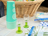 Picnic supplies for an RV rental trip: turquoise cups, green glasses, and paper plates on a plaid tablecloth.