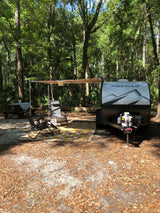 Experience tranquil nature with this Freesolo RV rental setup, featuring an awning, chairs, and picnic table at a shady forest campsite.