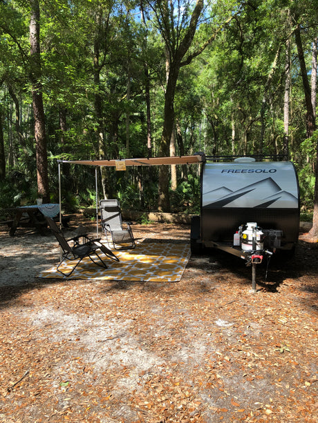 Experience tranquil nature with this Freesolo RV rental setup, featuring an awning, chairs, and picnic table at a shady forest campsite.