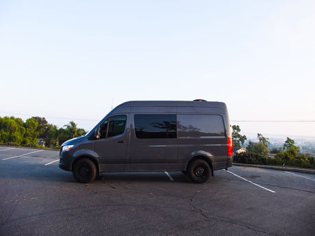 A sleek, dark gray camper van, a popular choice for an rv rental, parked on asphalt in an outdoor lot.