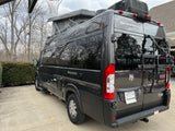 Dark gray Thor Sequence camper van RV rental, with a pop-top and rear bike rack, parked on a driveway.