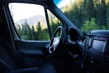 Inside an RV rental, showcasing its steering wheel, dashboard, and a stunning mountain forest view.