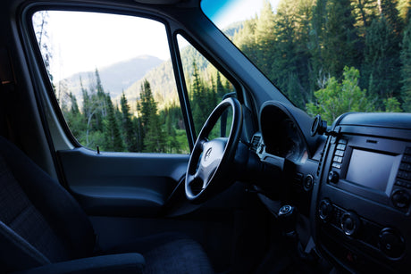 Inside an RV rental, showcasing its steering wheel, dashboard, and a stunning mountain forest view.
