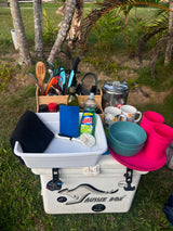 RV rental ready! Organized outdoor kitchen setup on a cooler, with cooking tools, dishware, and cleaning supplies for camp meals.