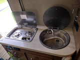 RV rental kitchen view: a practical setup with a two-burner gas stove and a stainless steel sink, both with protective lids.