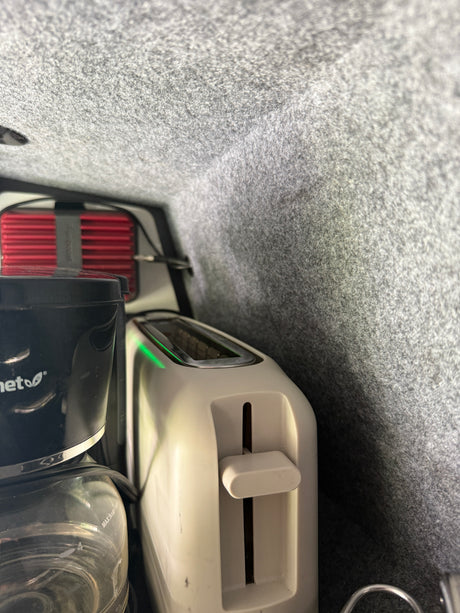 Compact kitchen setup in an RV rental, featuring a coffee maker and a toaster, neatly stored within a carpeted compartment.