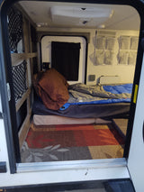 RV rental interior: bed, hanging organizers, and under-bed storage nets for compact living, viewed from the rear hatch.