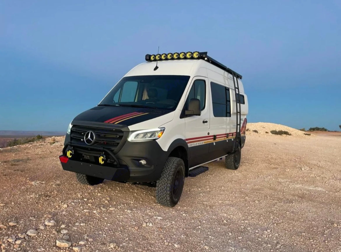 A rugged white Mercedes Sprinter adventure van, equipped for off-road travel, parked on a dirt road. Great for an RV rental.