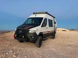 A rugged white Mercedes Sprinter adventure van, equipped for off-road travel, parked on a dirt road. Great for an RV rental.