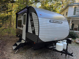 This Sun Lite LTD travel trailer, possibly an RV rental, is parked in a wooded area with its awning extended and propane tanks visible.